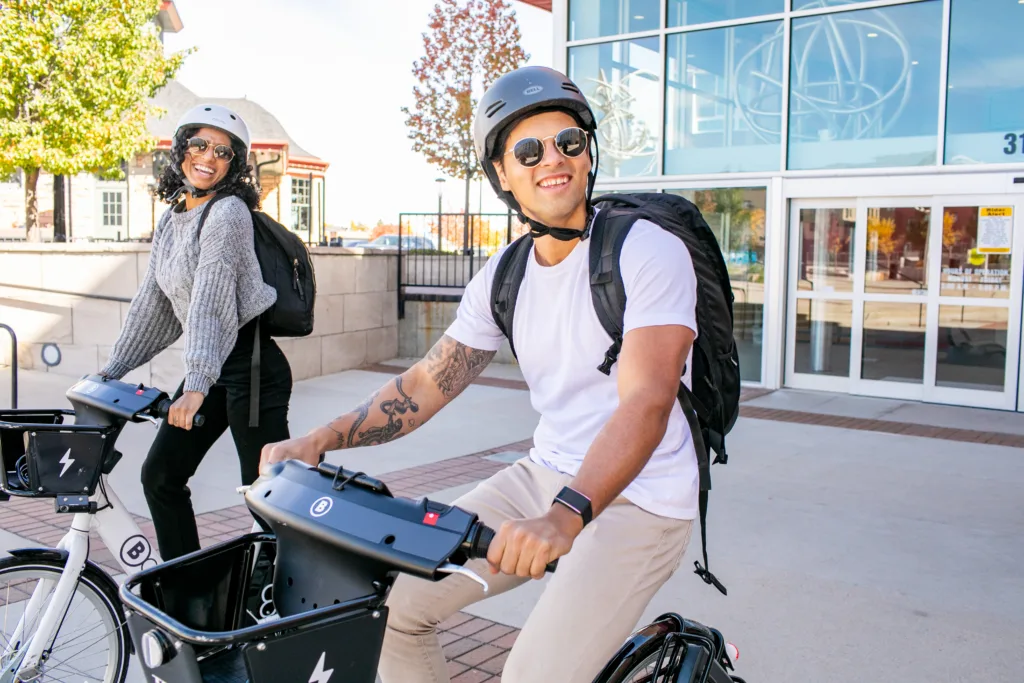 two friends riding bike share bicycles with big smiles
