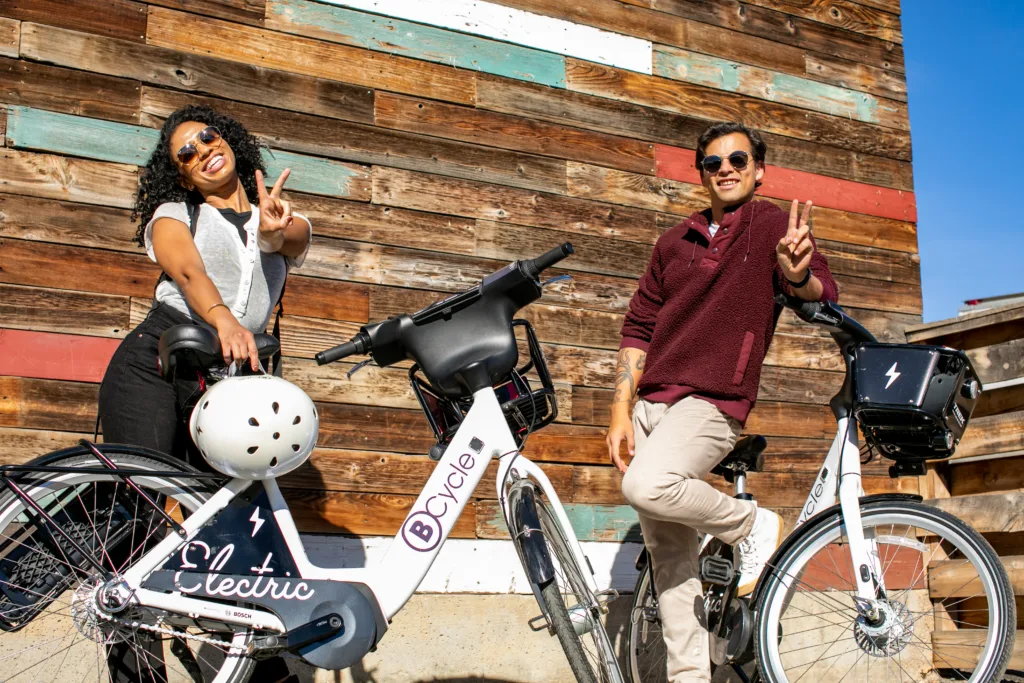 Photo of woman and man shooting the peace sign to the camera next to their bike share bicycles