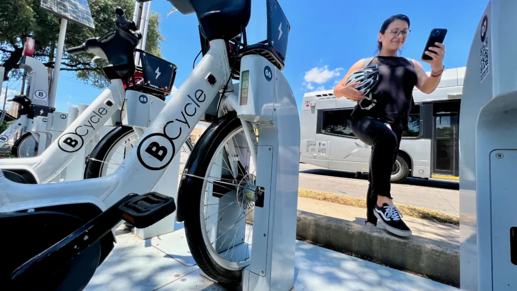 Latina woman using her smart phone to navigate the bike share system after stepping off a bus