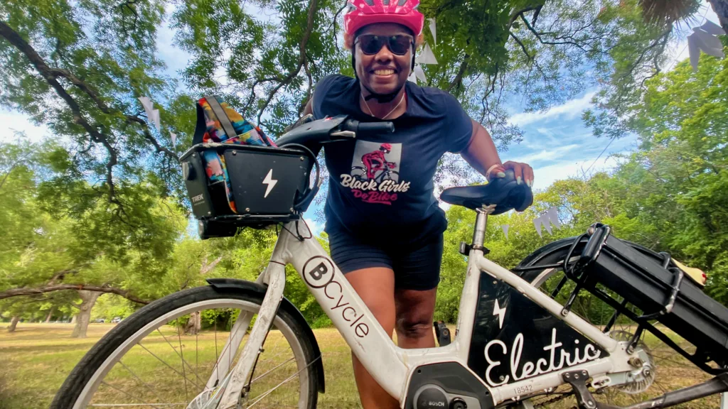 Black Girls Do Bike member leaning over a bike share bicycle smiling at the camera
