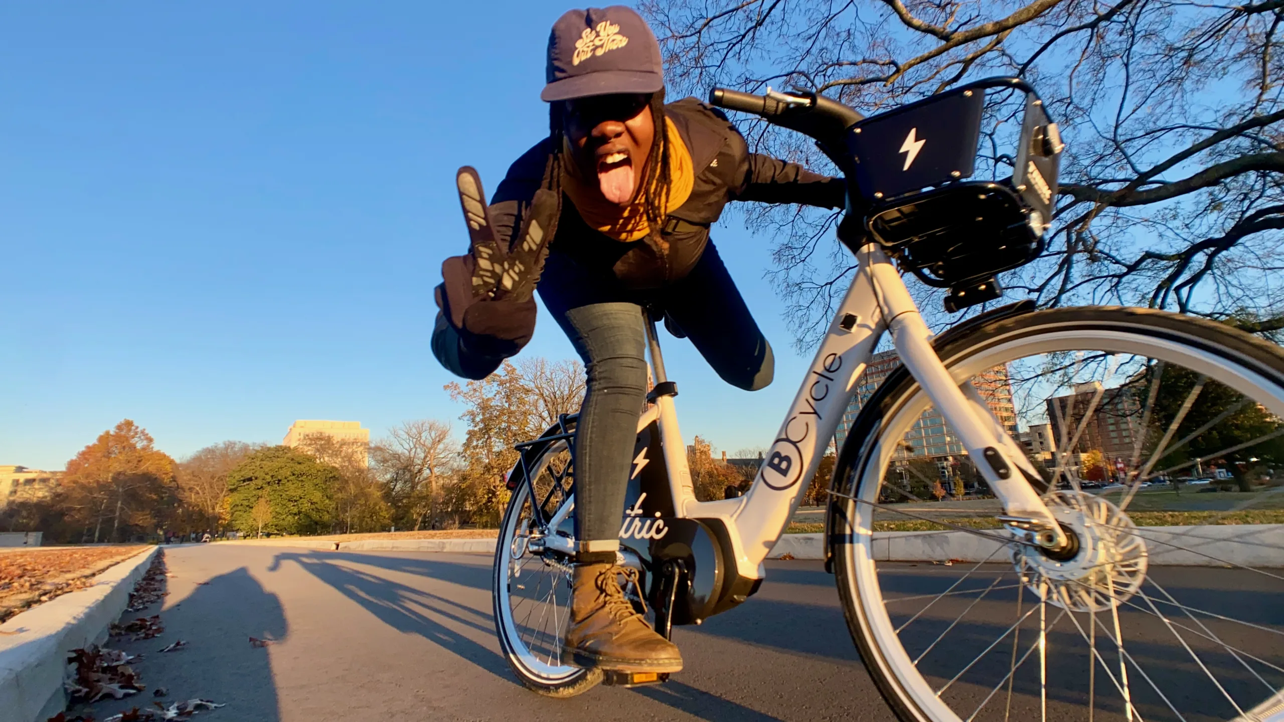 Woman riding a bike share bicycle giving the camera a peace sign as she rides by